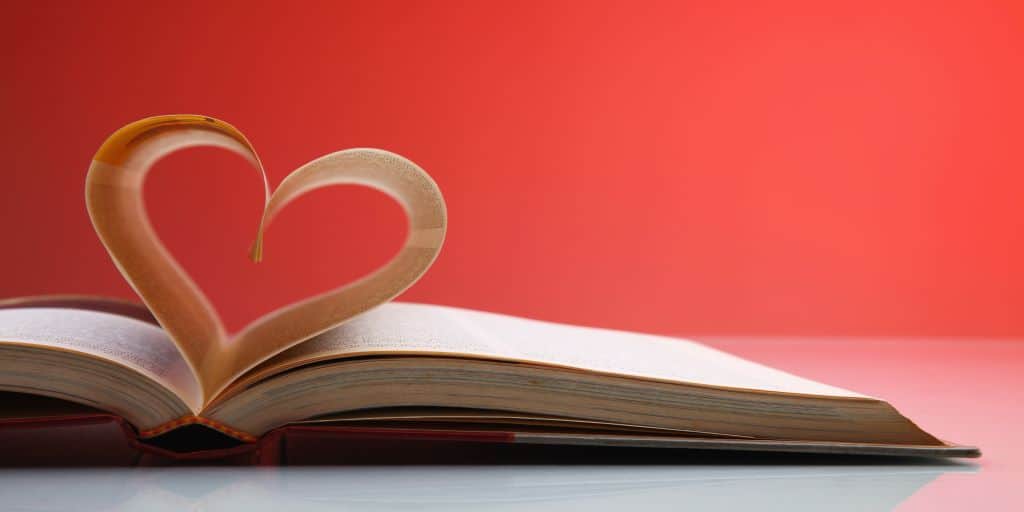 An open book with two pages curled into the shape of a heart, set against a rosy background to remind us that we can learn about God's love in His Word.